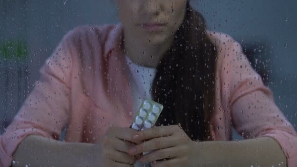 雨の窓、病気の近くに錠剤のブリスターパックを保持している落ち込んだ孤独な女性 — ストック動画