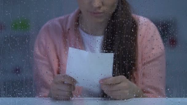 Καταθλιπτική γυναίκα κρατώντας σχισμένη φωτογραφία κοντά σε βροχερό παράθυρο, υποφέρει οδυνηρό διαζύγιο — Αρχείο Βίντεο