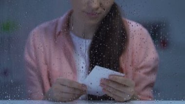 Yağmurlu pencerenin yakınındaki fotoğrafa bakan üzgün genç kadın, boşandıktan sonra kayıp çocuk