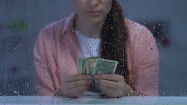 Pensive poor middle-aged female counting dollar cash and looking in rainy window — Stock Video