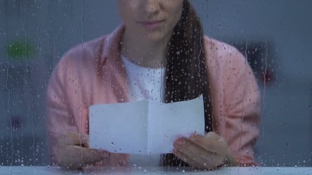Upprörd ensam dam sitter bakom regniga fönster och läsa brev, saknade familj — Stockvideo