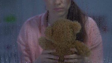 Yanağında yara ile üzgün kadın sarılma oyuncak ayı, mutlu çocukluk hatırlayarak