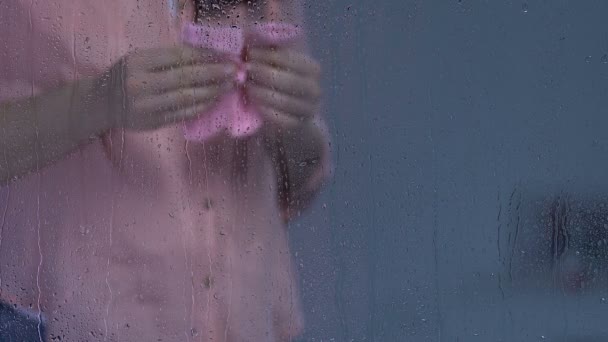 Беременная женщина держит розовые носки и трогает живот за дождливым окном, угроза — стоковое видео