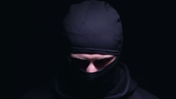 Bandit in balaclava looking at camera, alarm flashlight on dark background — Stock Video