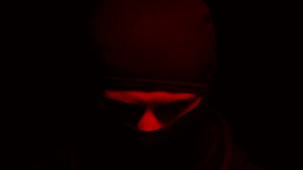 Criminal en pasamontañas mirando a la cámara, linternas rojas sobre fondo negro — Vídeo de stock