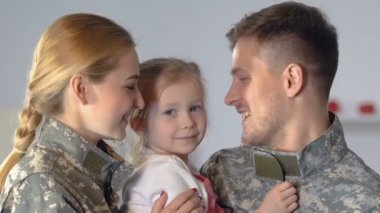 Young parents in camouflage uniform kissing daughter cheek, family closeness