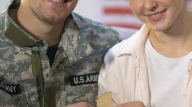 Wife and husband military uniform holding wooden house sign, ownership, mortgage