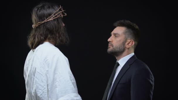 Мессия в терновом венце обнимает плачущего мужчину на темном фоне, поддерживает — стоковое видео