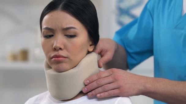 Doctor applying foam cervical collar to female, uncomfortable medical support — Stock Video