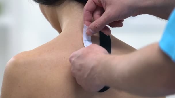 医師は女性の上背部にY字型のテープを塗布し、筋肉の緊張を軽減 — ストック動画