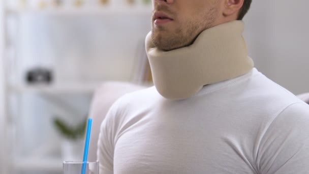 Man in foam cervical collar trying to drink water with straw, discomfort — Stock Video