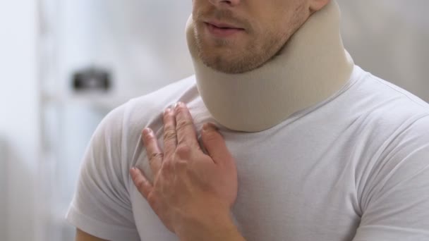 Male in foam cervical collar massaging painful shoulder and neck, trauma — Stock Video