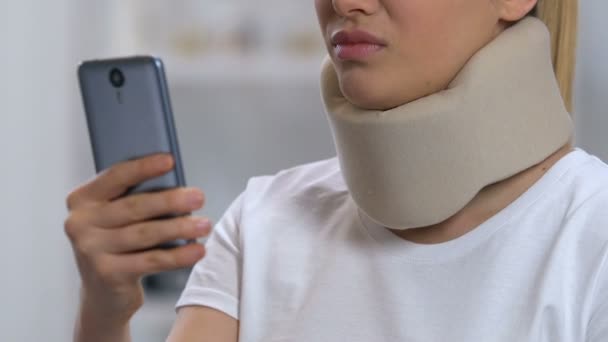 Lady with smartphone in foam cervical collar feeling neck pain, rehabilitation — Stock Video