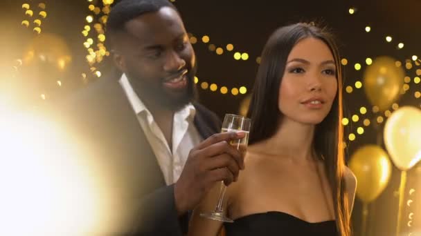 Smiling afro-american male offering dancing lady glass of champagne, flirt — Stock Video