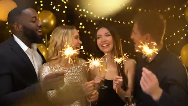 Feliz grupo de amigos sosteniendo luces de bengala y copas de vino, saludo de Año Nuevo — Vídeos de Stock