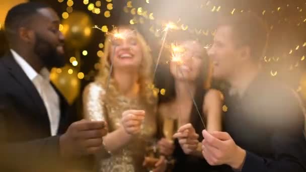Cuatro colegas alegres sosteniendo bengalas ardientes y copas de champán, fiesta — Vídeos de Stock