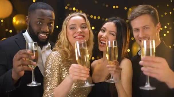 Jóvenes amigos felices brindando en la cámara sosteniendo gafas luces festivas de fondo — Vídeos de Stock