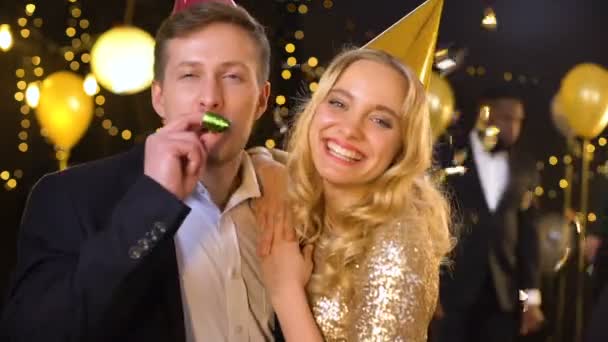 Opgewonden paar glimlachend op camera staande vallende confetti, blazen partij hoorn — Stockvideo