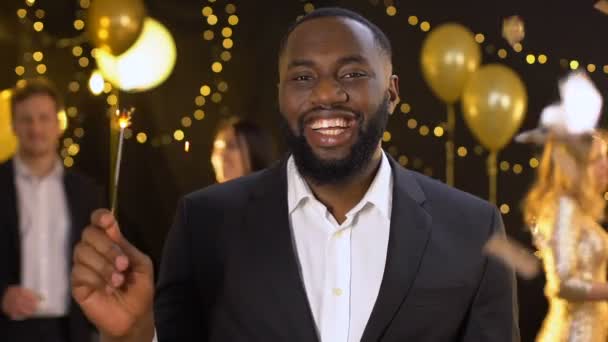Joyful black male holding bengal light in hand smiling camera, festive event — Stock Video