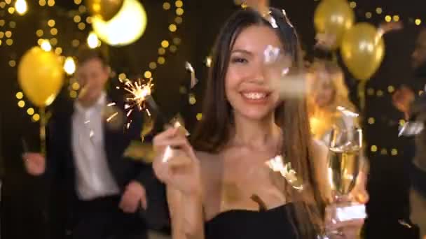 Positive woman winking camera holding champagne glass sparkler falling confetti — Stock Video