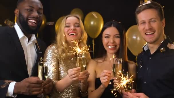 Smiling friends with champagne and bengal lights standing under falling confetti — Stock Video