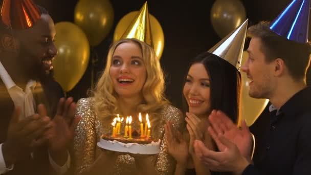 Gelukkig Kaukasische vrouw in b-day Hat blowing kaarsen op taart, vrienden applauderende — Stockvideo