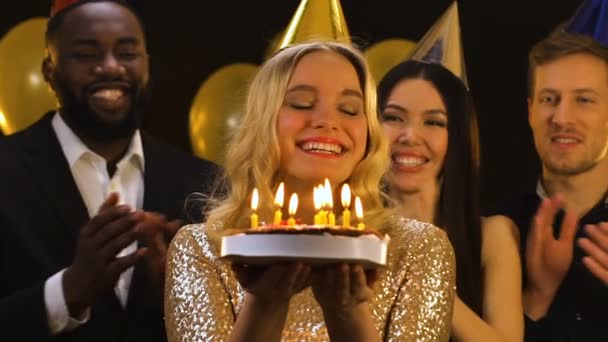 Alegre dama caucásica soplando velas en pastel de cumpleaños, amigos aplaudiendo — Vídeo de stock