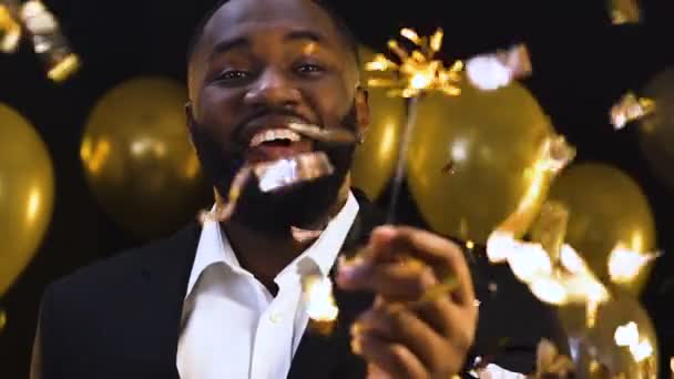 Happy афро-американський чоловік розмахуючи бенгальським світлом під падінням конфетті, партія — стокове відео