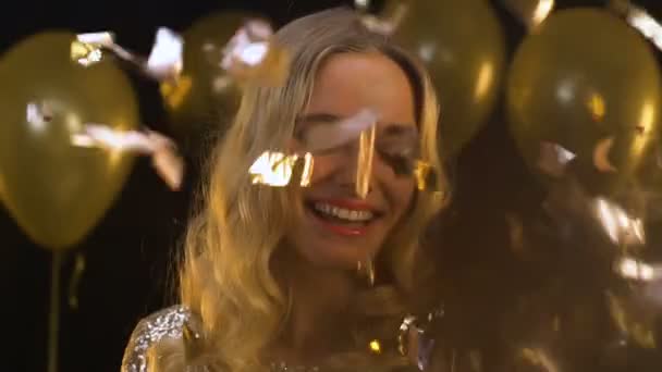 Sorrindo mulher loira com taça de champanhe de pé sob queda confetti, festa — Vídeo de Stock