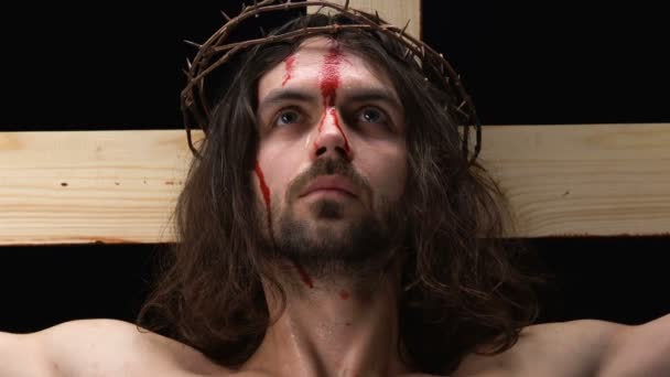 Piangendo Gesù Cristo con la faccia sanguinante guardando la macchina fotografica, la crocifissione sulla croce — Video Stock