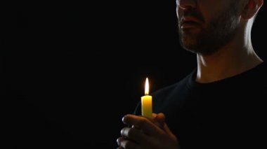 Mum tutan ve karanlık arka plana karşı dua eden adam, Tanrı'ya itiraf