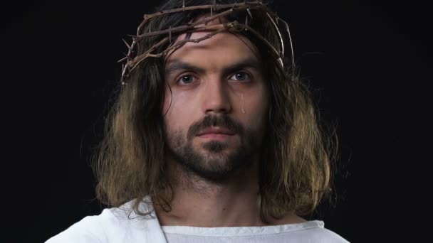 Crying Jesus Christ in crown if thorns looking at camera against dark background — Stock Video