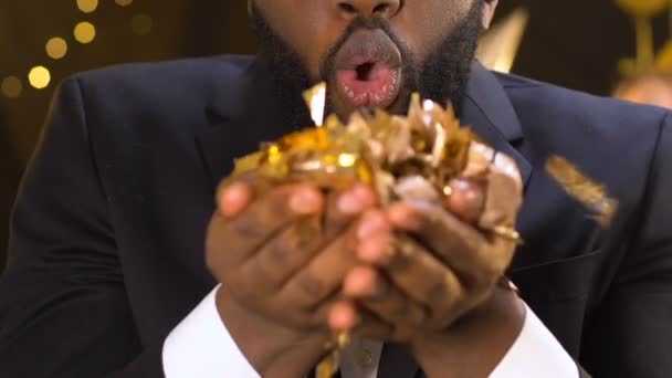 Радісний афроамериканський чоловік, який дме на конфетті і танцює на вечірці, святкування — стокове відео