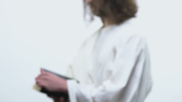 Hombre con túnica blanca abriendo la Biblia y mirando a la cámara, responde con fe — Vídeo de stock