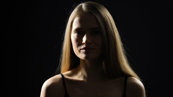 Genç kadın kameraya yüz çevirerek ve gülümseyen, kadınlık, siyah arka plan — Stok video