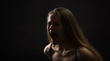 Kadın karanlık arka plan aleyhine bağırıyor, el ile ağız kapatarak, sakinleştirici