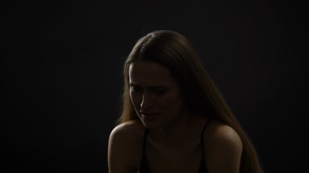 Плачуча дама сидить на самоті на темному тлі, страждає від життєвих проблем — стокове відео