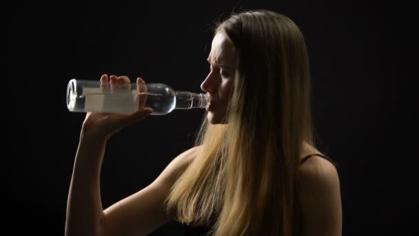 Young woman drinking alcohol from bottle and crying against dark background — Stock Video
