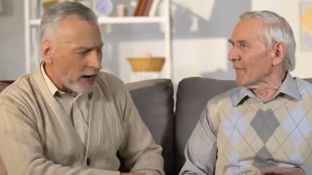 Старшие мужчины спорят сидя на диване, друзья недоразумение, общение — стоковое видео