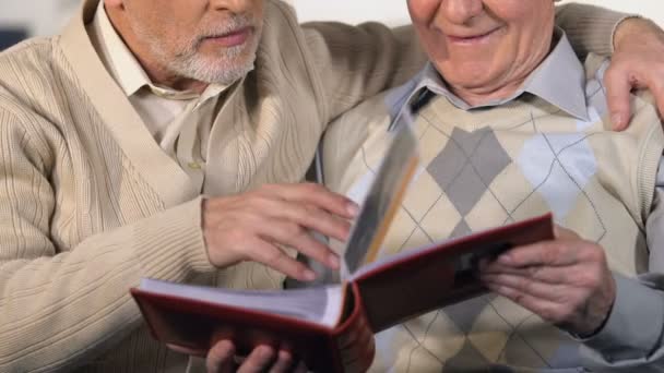 Зрілі пенсіонери дивляться фотоальбом і посміхаються, насолоджуючись разом — стокове відео