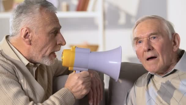 Hombre anciano escuchando a un amigo gritando en megáfono, sordera enfermedad, salud — Vídeo de stock
