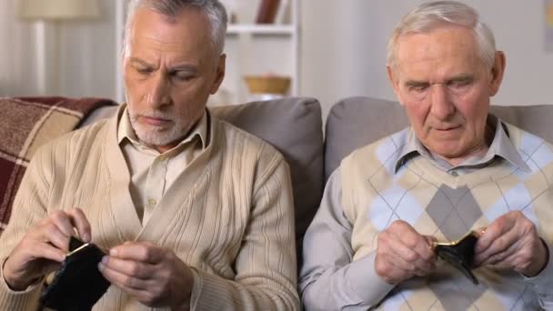 Нещасливі чоловіки похилого віку дивляться порожні гаманці, пенсійна бідність, пенсійні заощадження — стокове відео