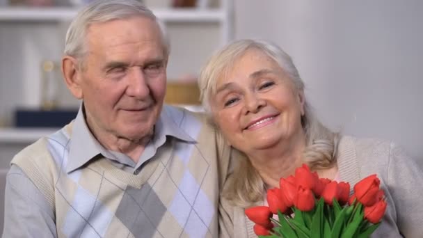 Sonriendo pareja anciana abrazando, mujer oliendo flores, celebrando aniversario — Vídeos de Stock