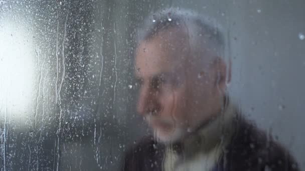 Грустный мужчина-пенсионер чувствует себя одиноким, дождь капли стекла окна, меланхолия, проблема — стоковое видео