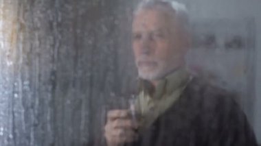 Emekli erkek tadı viski ev, yağmurlu pencere dışarı bakarak zevk