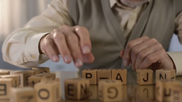 Male pensioner trying to make word of wooden cubes, old age dementia, rehab — Stock Video