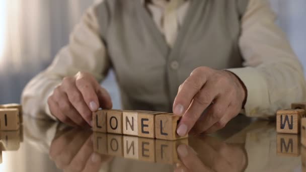 Aposentado enrugado fazendo palavra solitário de cubos de madeira na mesa, lar de idosos — Vídeo de Stock