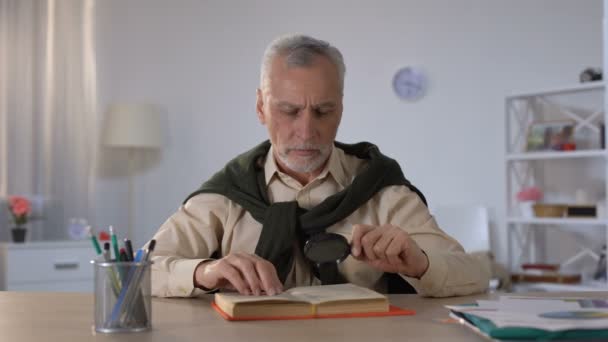 Старший чоловік читає книгу зі збільшувальним склом, увагою до деталей, ерудицією — стокове відео