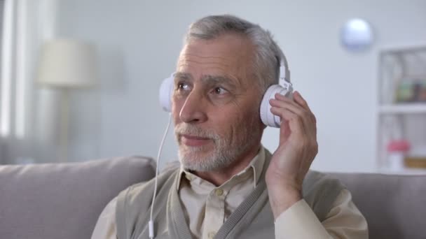 Позитивный пенсионер в наушниках слушает музыку, наслаждается любимым радио — стоковое видео