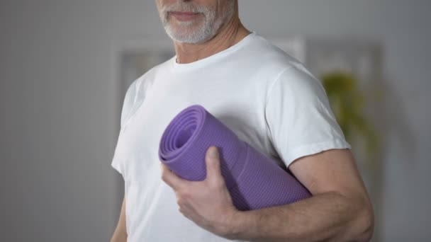 Пенсіонер тримає йогу килим, концепція тренувань і здорового способу життя в літньому віці — стокове відео